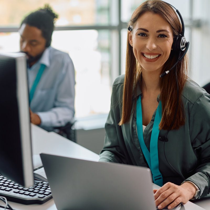 Happy customer service representative working at call center office and looking at camera.